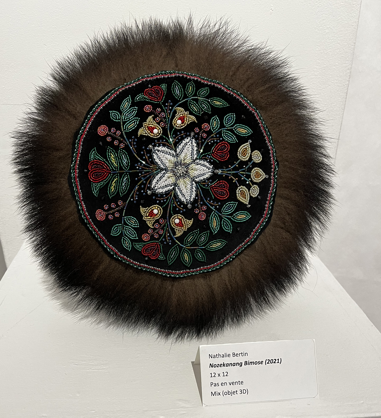 Un tissage de fleurs et feuillages en perles sur fond noir, entouré d'une fourrure brune.